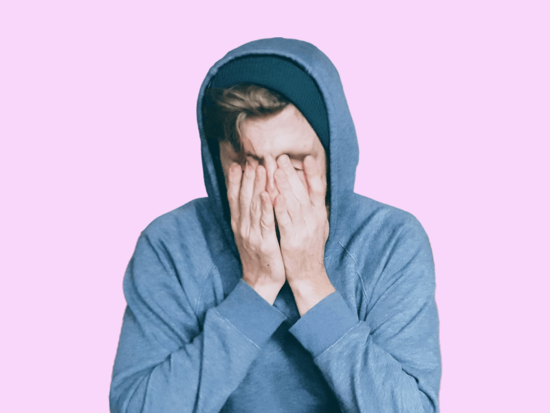 stressed student in blue hoodie covering face with hands on pink background