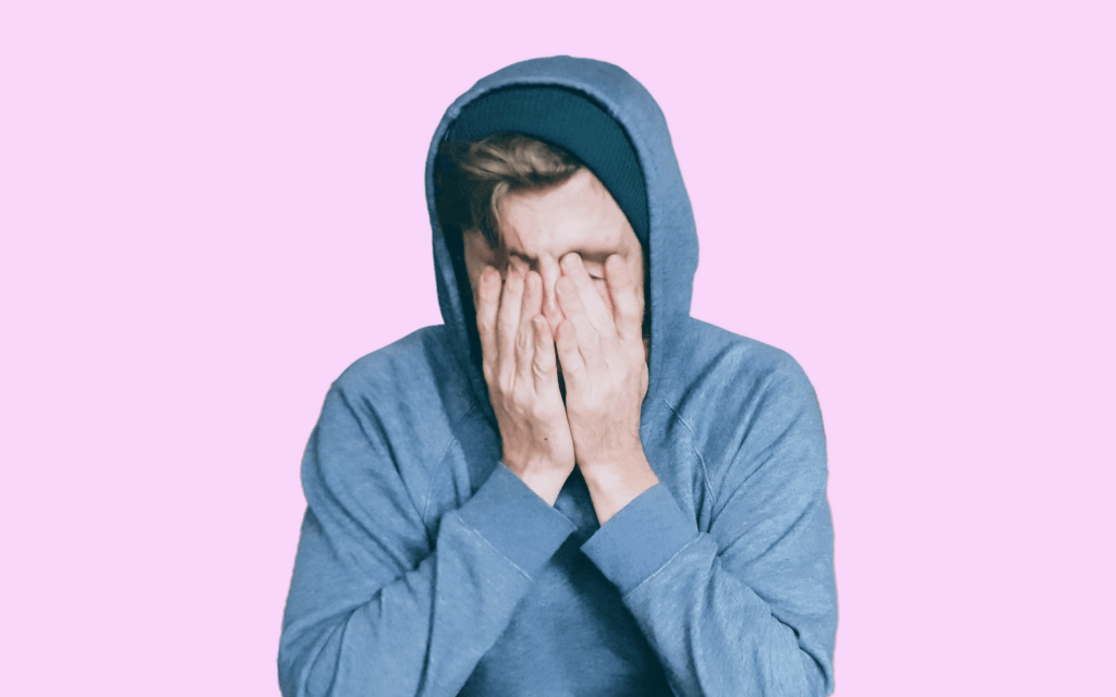 young person in a hoodie covering their face with both hands, illustrating the emotional exhaustion of gifted kid burnout