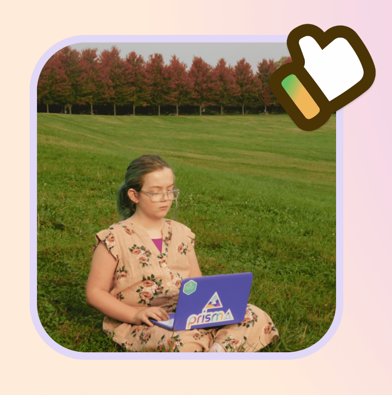 young student sitting on grass outdoors using a Prisma laptop for online learning