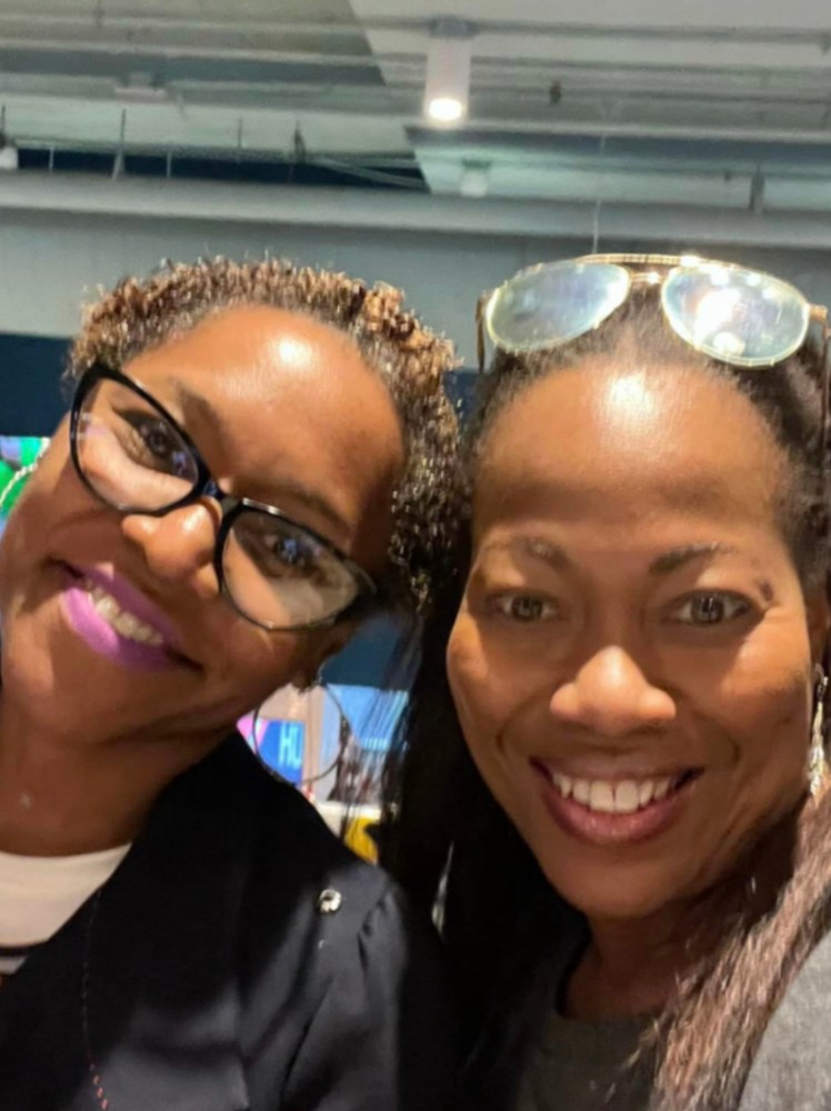 two smiling Prisma family members taking a selfie together at an indoor event