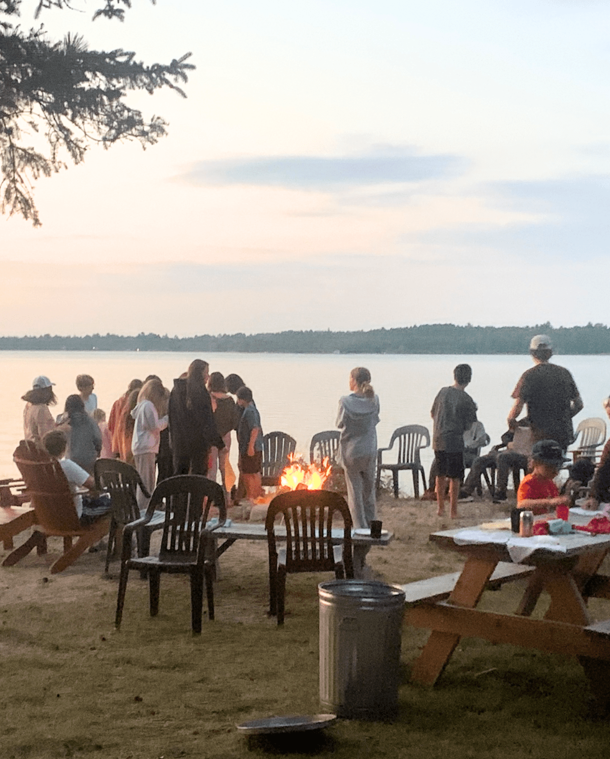 Prisma families gathering around a lakeside campfire at sunset