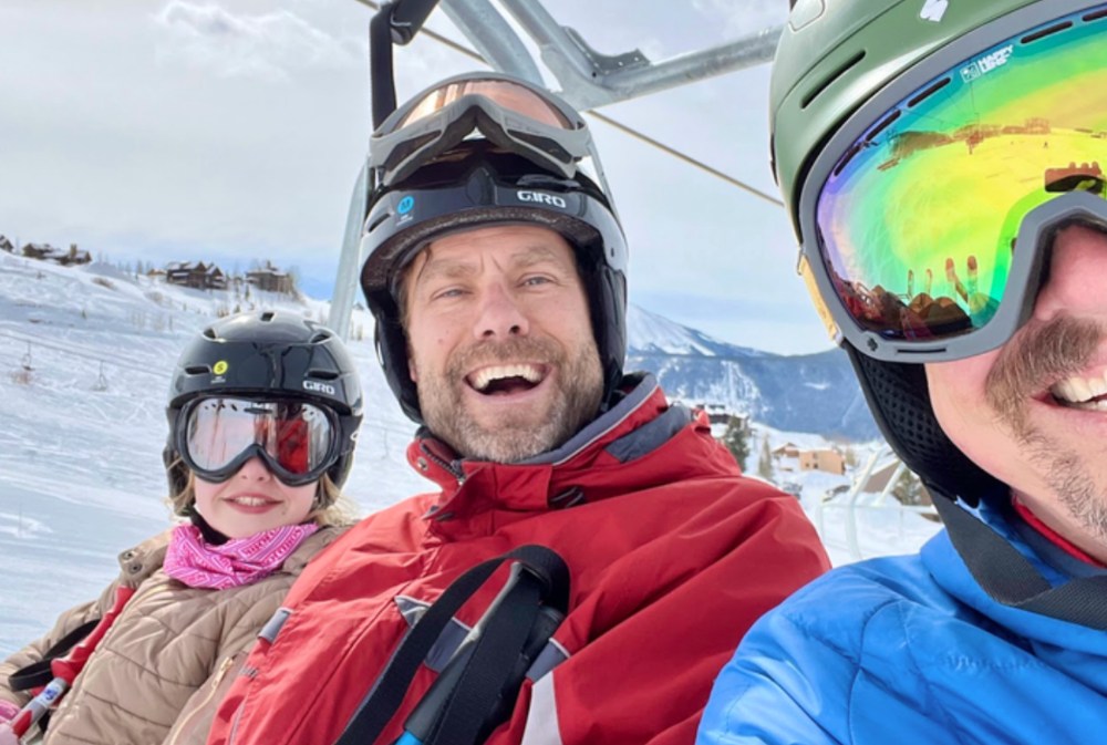 Prisma family selfie on a ski lift with snowy mountain slopes in the background