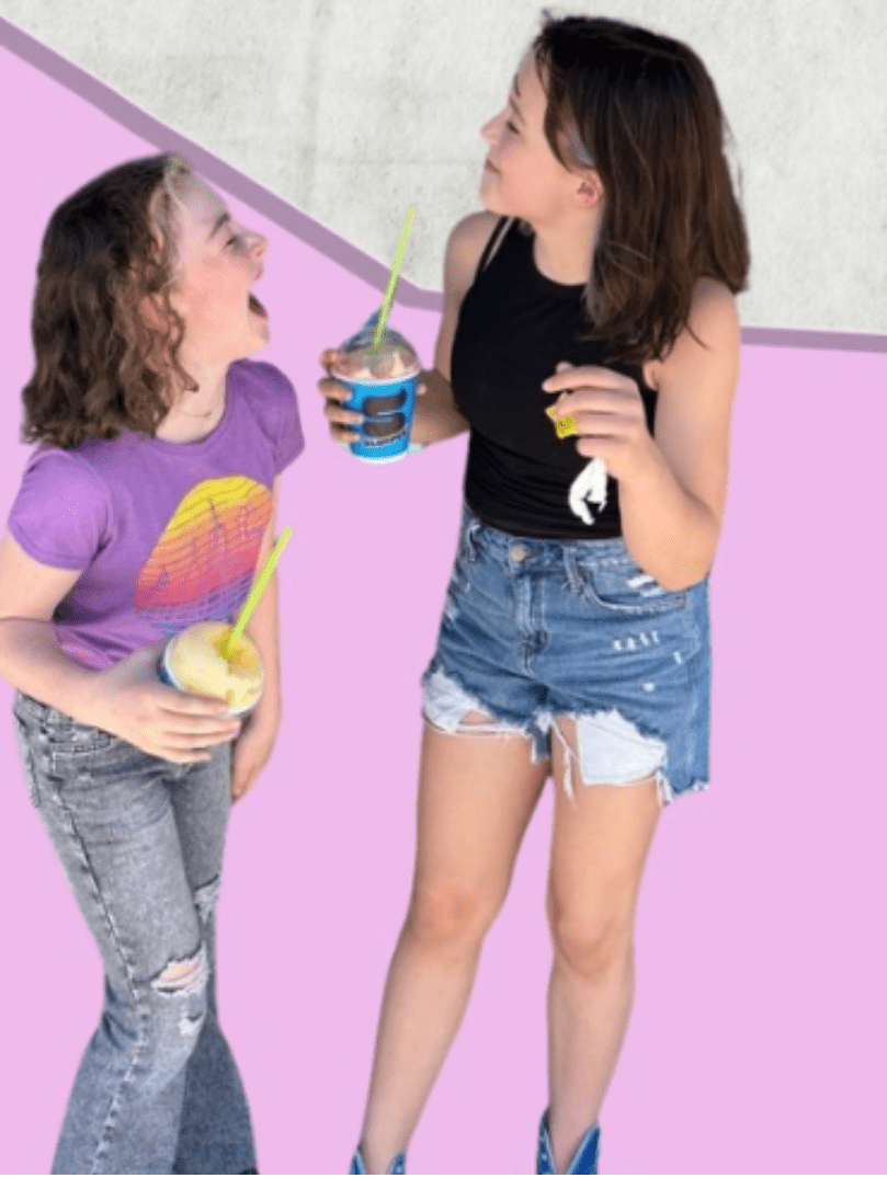 two Prisma middle school students laughing together while holding frozen drinks