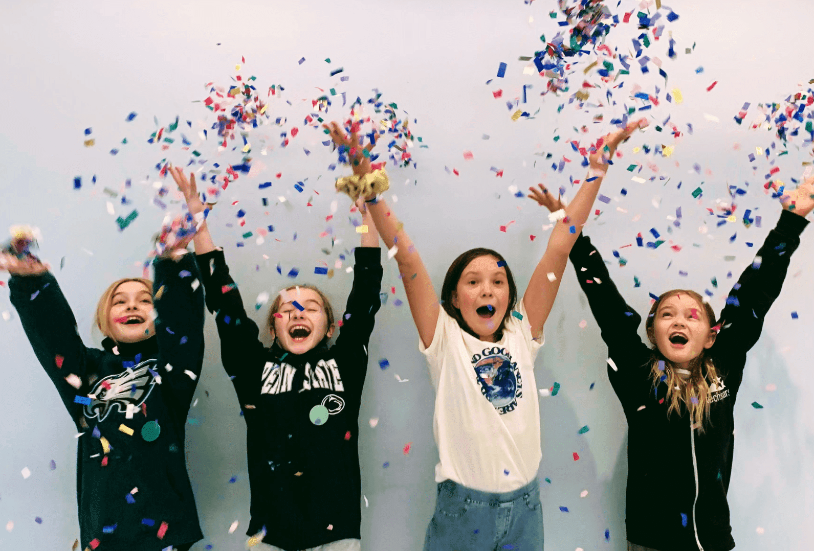 four Prisma students celebrating with arms raised throwing colorful confetti