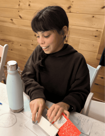 smiling Prisma student writing and crafting with paper at a wooden table