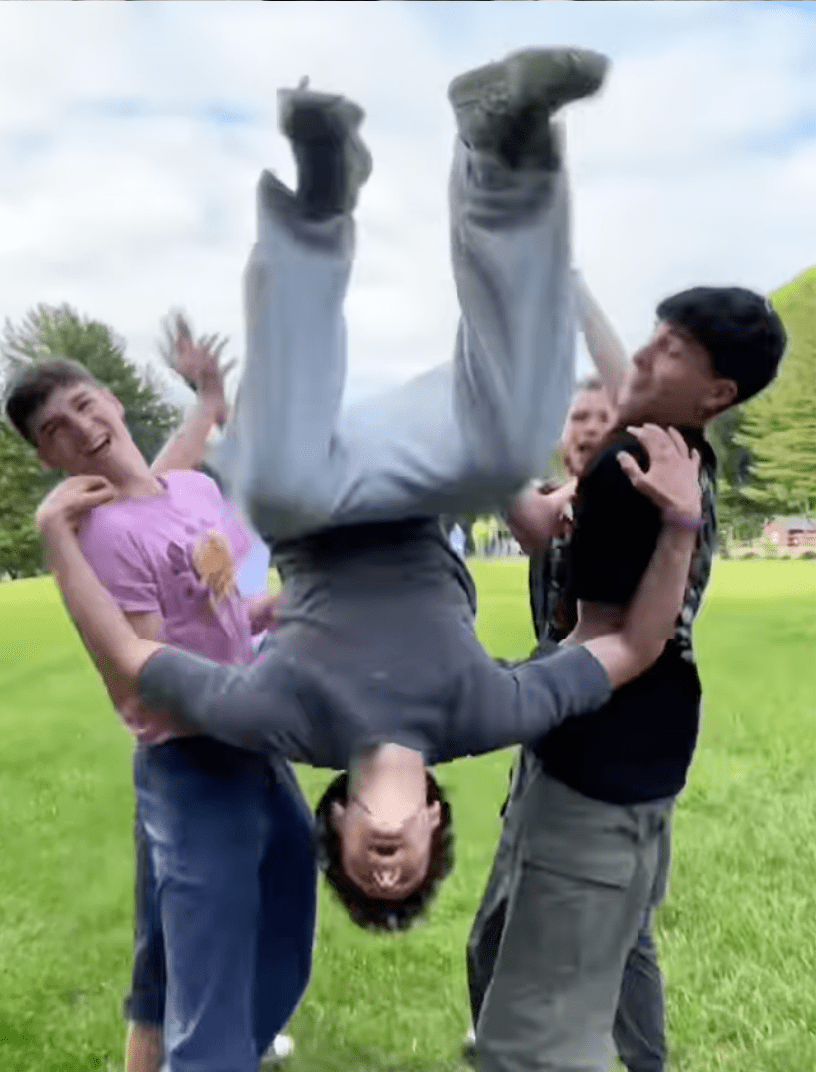 Prisma learners playfully lifting a friend upside down on a green lawn outdoors