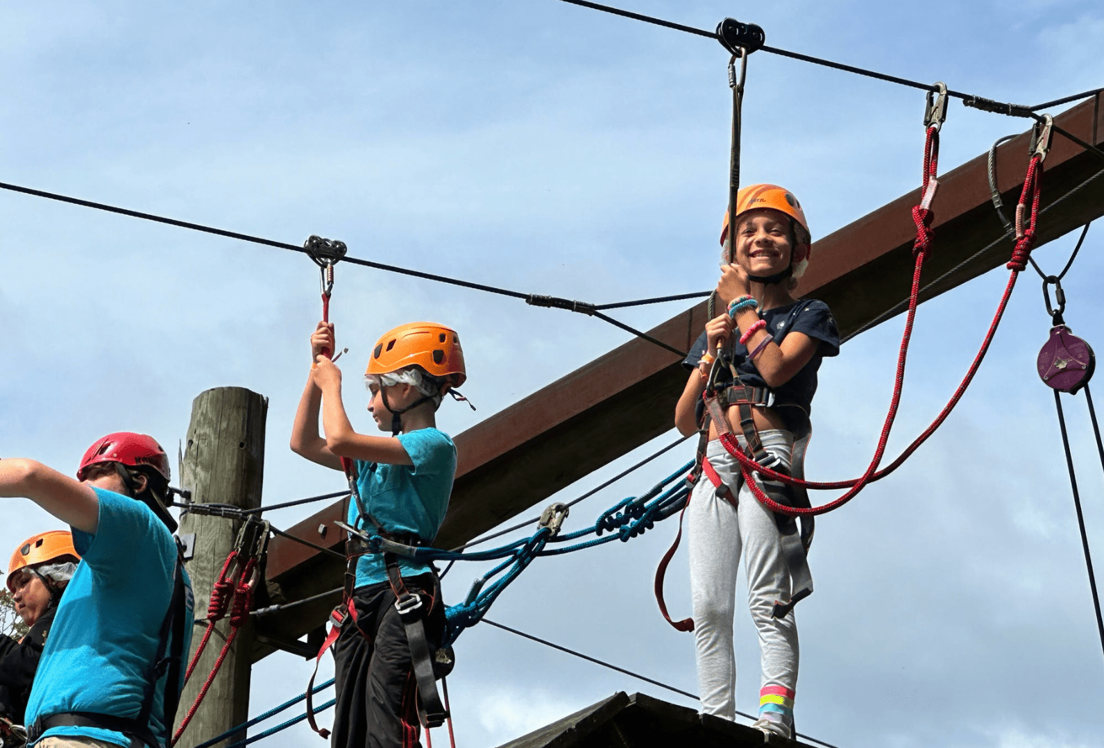Prisma kids wearing helmets and harnesses smiling on a high ropes adventure course