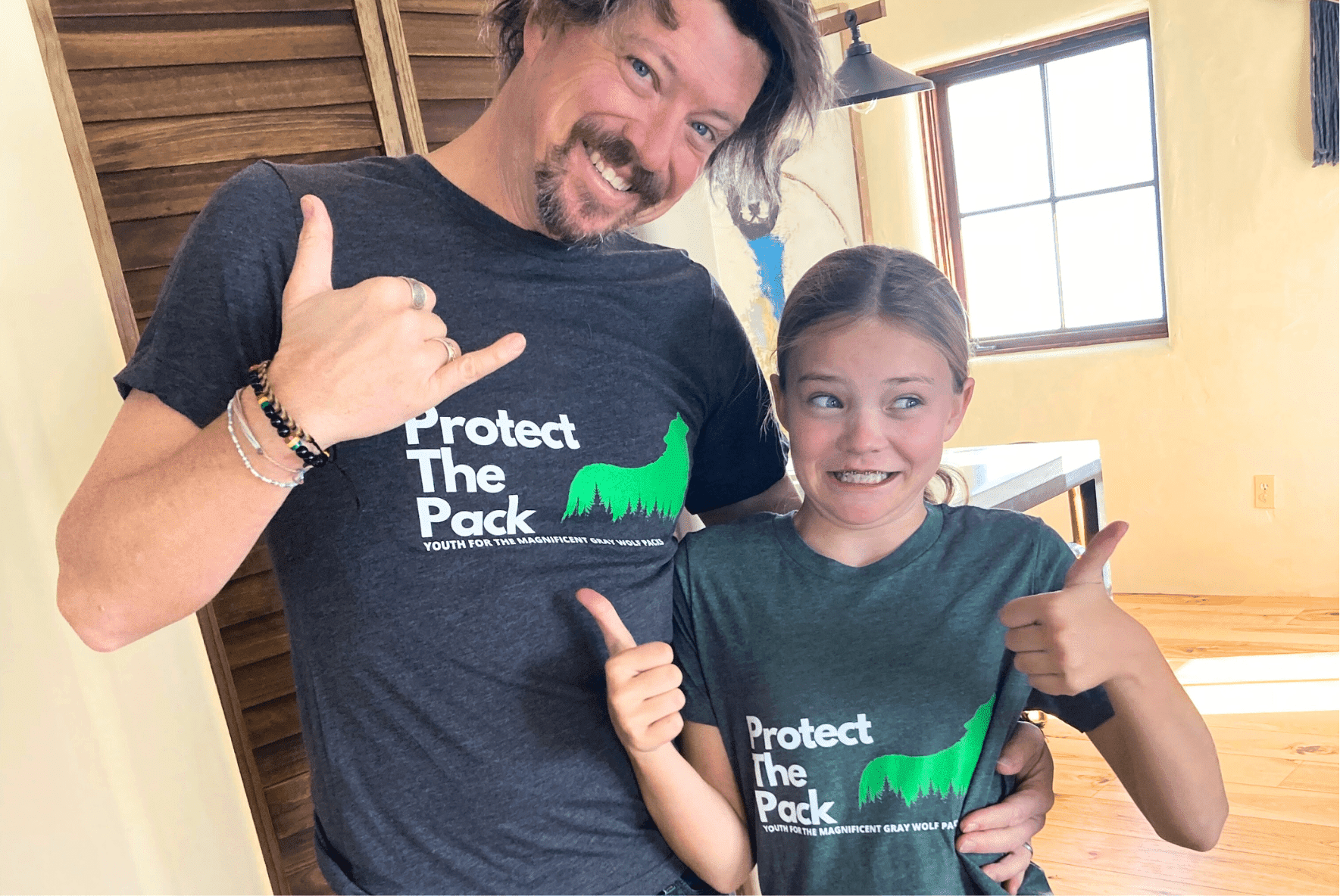 Prisma student and parent wearing matching Protect The Pack wolf conservation t-shirts giving thumbs up