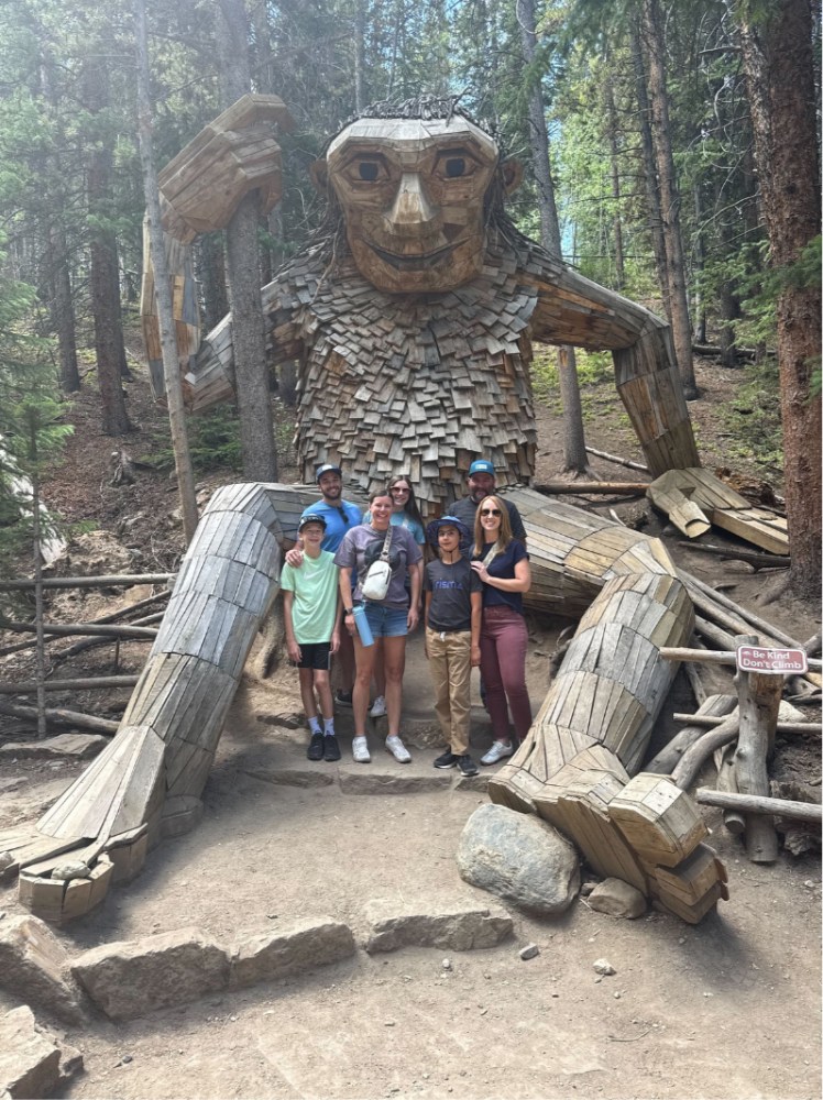 Prisma family group posing in front of a giant wooden troll sculpture in a forest