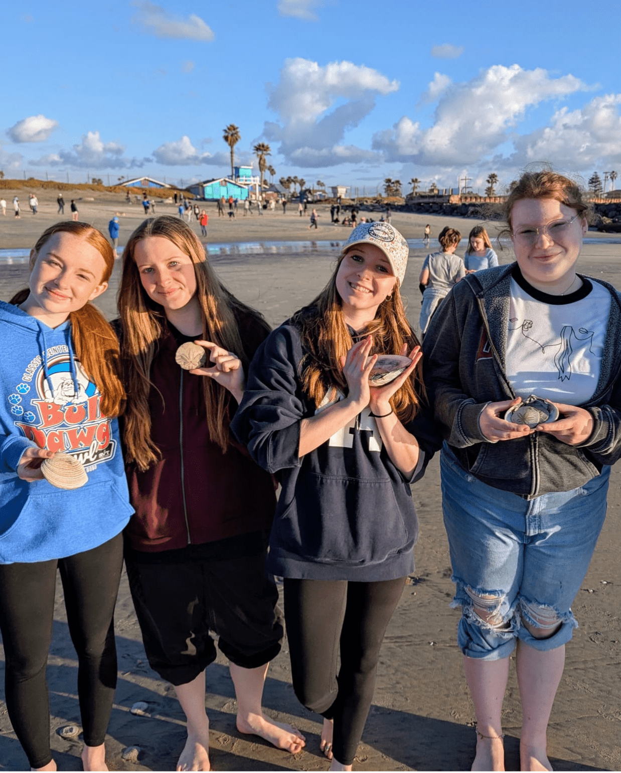 four Prisma high school students holding rocks and smiling together on a beach