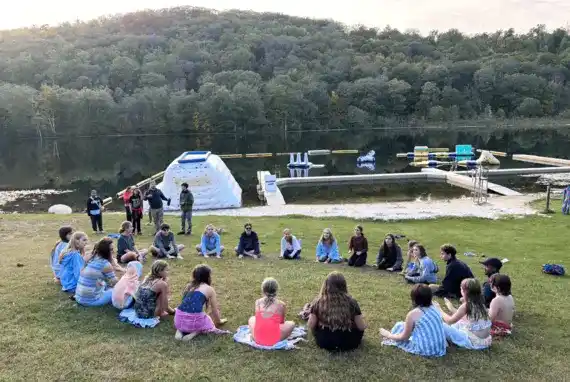 Prisma students sitting in a circle on grass by a lake during an outdoor homeschool meetup