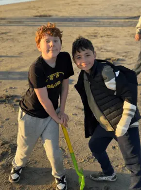 two Prisma students posing together outdoors on a sandy beach