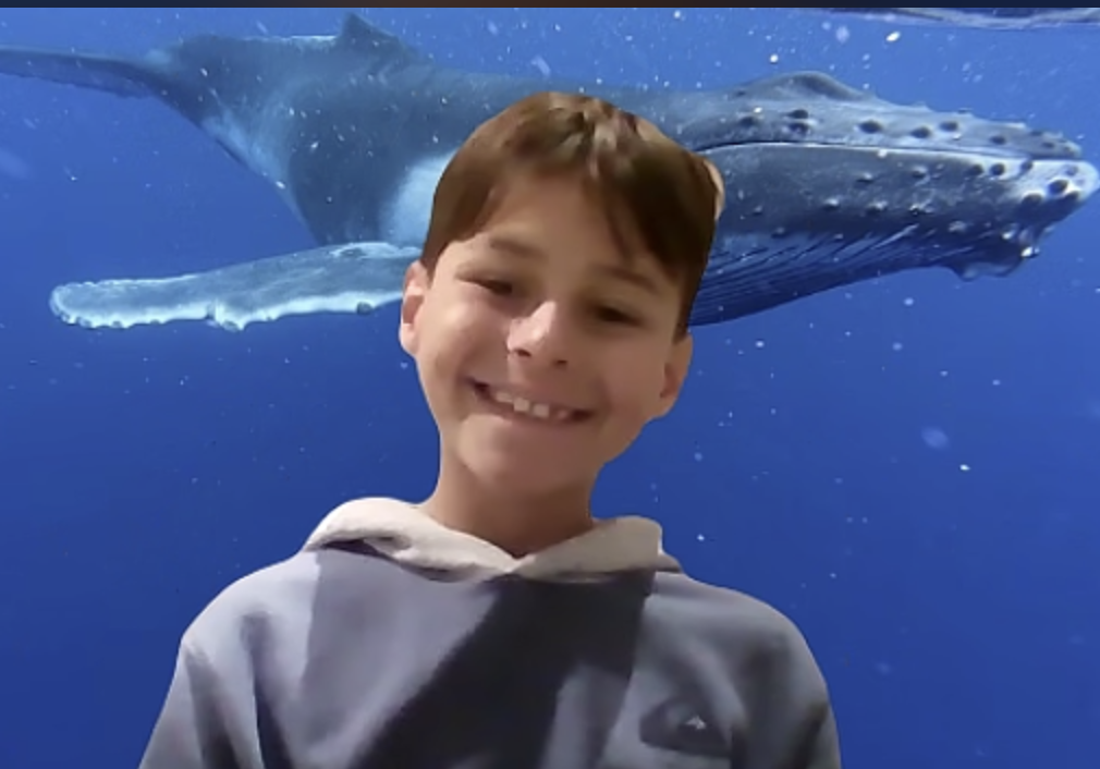 smiling Prisma lower school student on a video call with a whale background