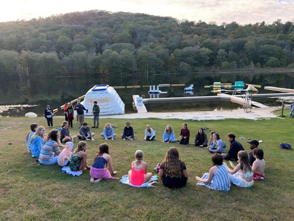 Prisma students sitting in a circle on grass by a lake during an outdoor homeschool meetup
