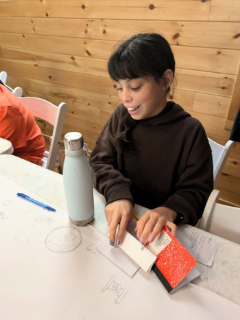 smiling Prisma student writing and crafting with paper at a wooden table