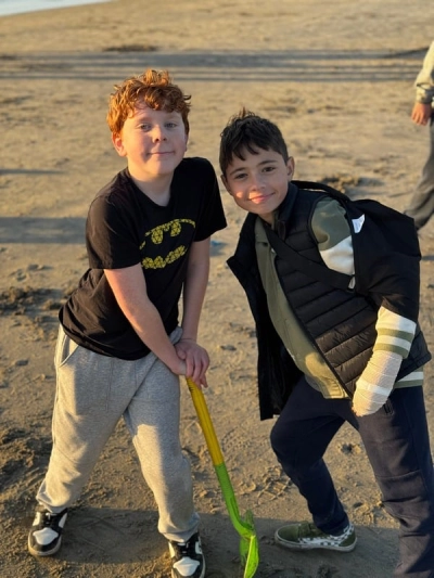 two Prisma students posing together outdoors on a sandy beach